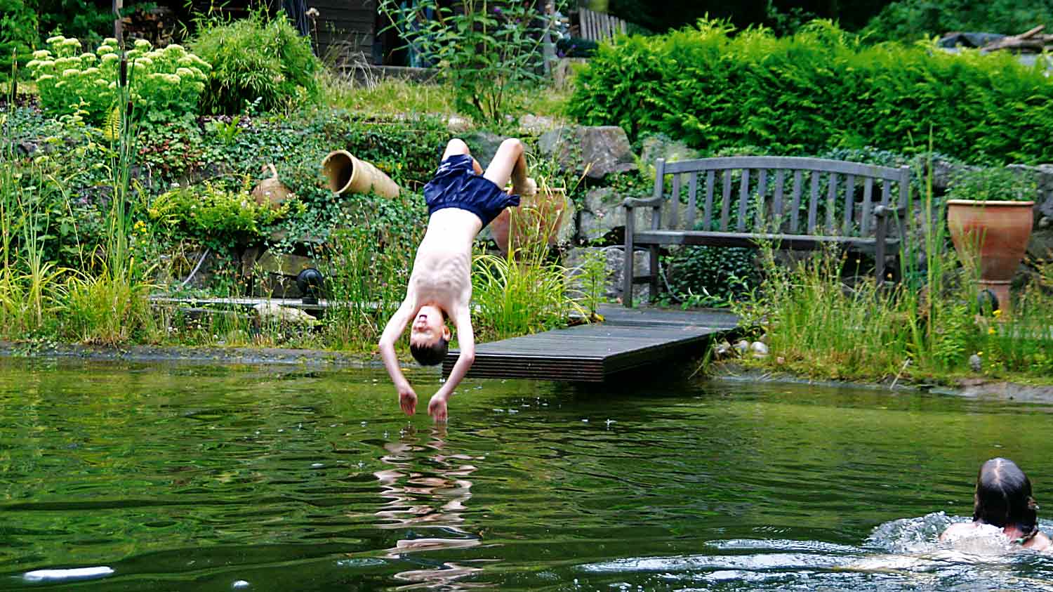 Ein Junge springt mit einem Rückwärtssalto in einen Schwimmteich