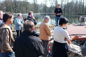 Dr. Holger Kraus führt die Gruppe zu den Trommelfiltern am Tauchpark. Er erläutert, was NaturaGart unternimmt, um das Wasser in dem riesigen Teich zu reinigen.
